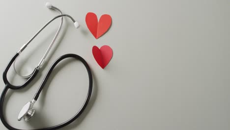 Video-of-stethoscope-with-two-red-paper-hearts-on-grey-background-with-copy-space