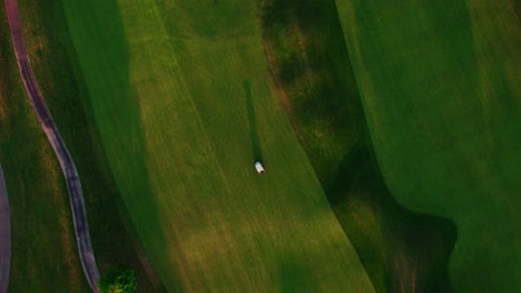 top-down-of-a-golf-cart,-aerial-rising-revealing-golf-terrain-in-the-evening