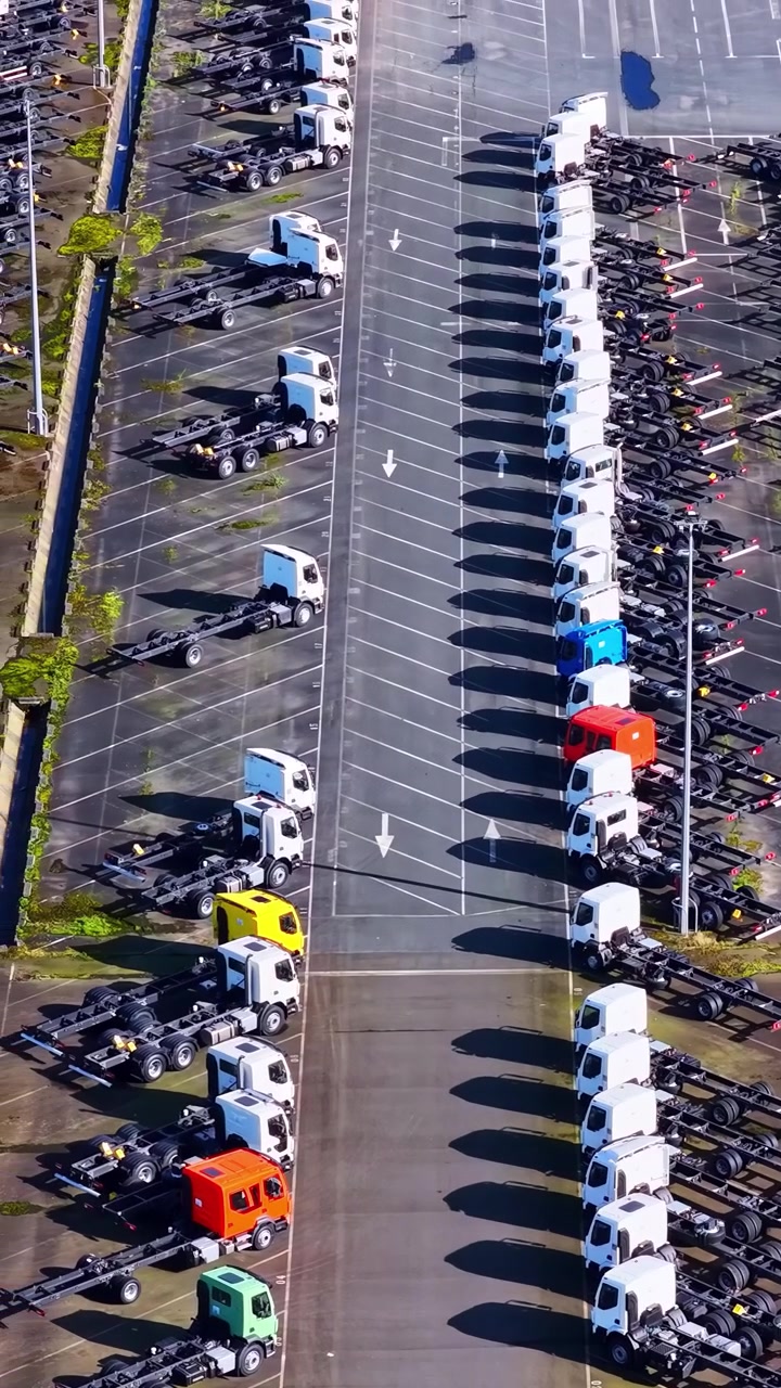 Vista aérea de filas de camiones nuevos estacionados en formación ordenada en un depósito de vehículos.