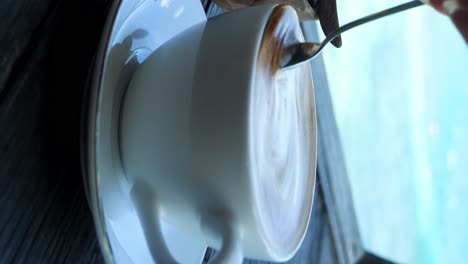 Static-slow-motion-close-up-shot-of-a-delicious-coffee-latte-from-bali-indonesia-with-the-beautiful-blue-sea-in-the-background-being-drunk-and-enjoyed-during-a-break-from-traveling