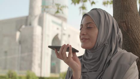 woman sitting near mosque and using telephone