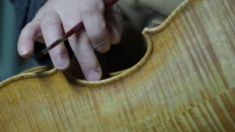 master luthier applying traditional varnish to a violin ribs of center bout with delicate precision and artistic skill