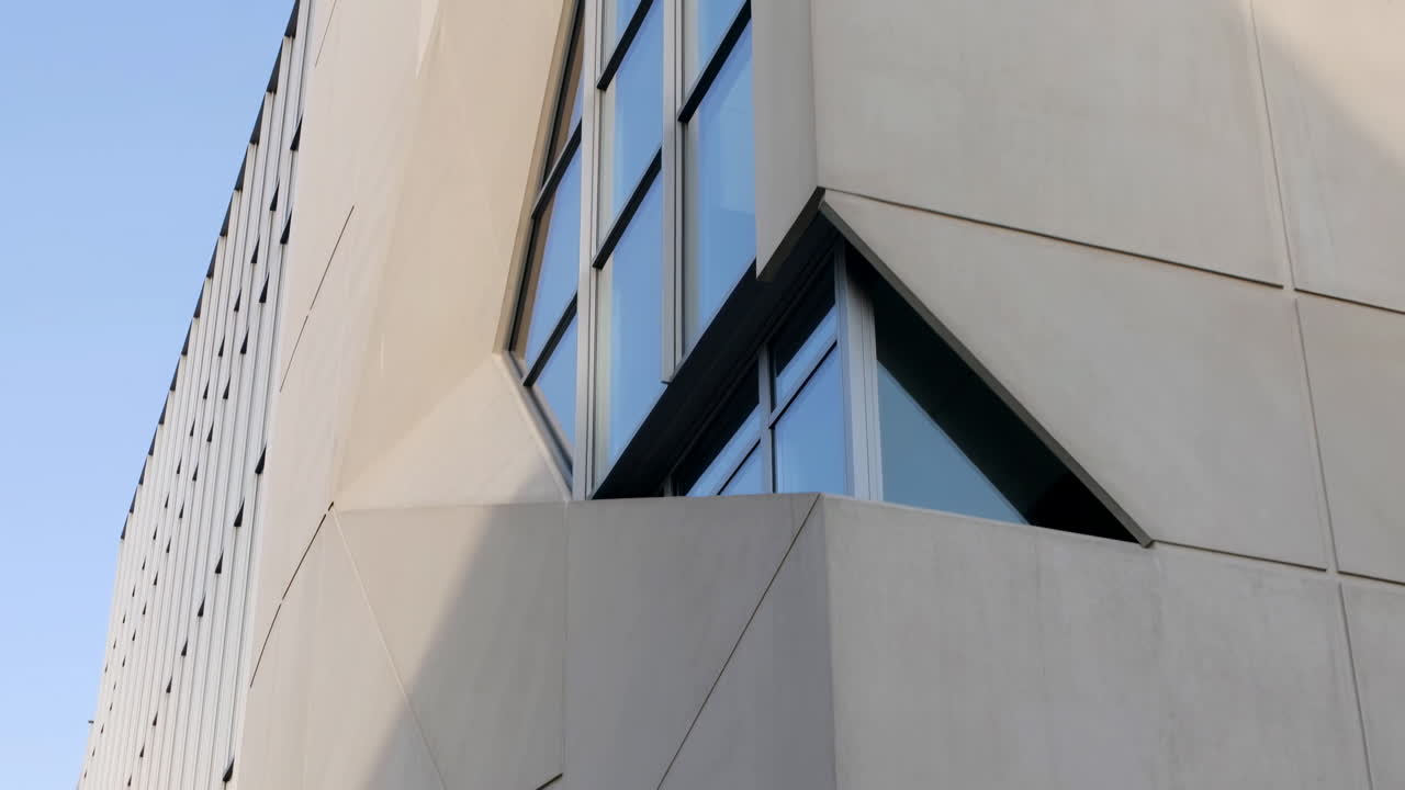 Panoramica verso l'alto della facciata di un moderno edificio geometrico con finestre riflettenti