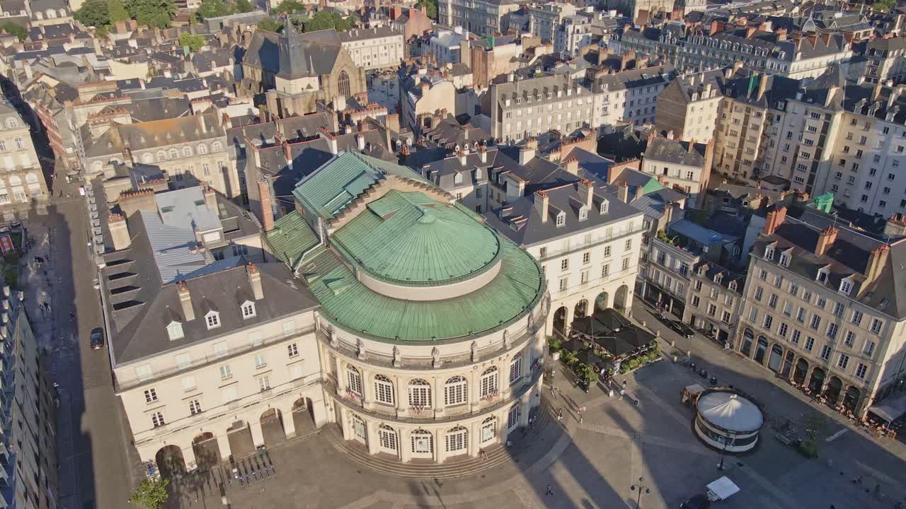Drone top-down shot of Rennes Opera with green roof, square, and city center at sunset.