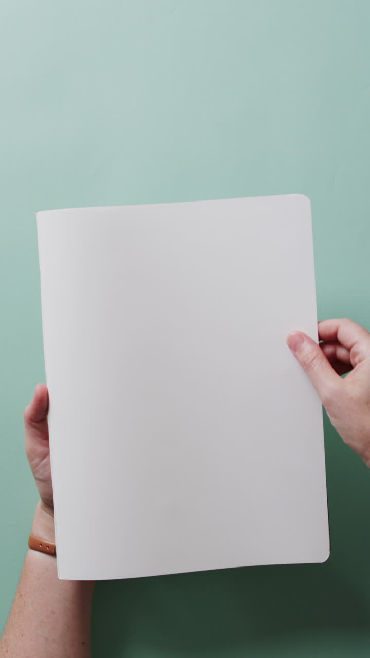 Vertical video of hand leafing through book with copy space on green background in slow motion