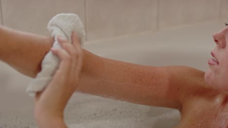 hermosa mujer relajándose en el baño usando un paño para limpiar su brazo