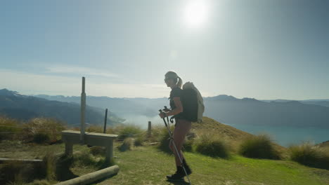 Lone-female-hiker-stepping-over-fence-on-mountain-trail-with-bright-sunshine