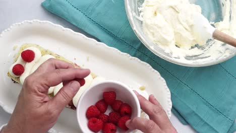 making a dessert called red raspberry tea cake made with fresh berries and vanilla buttercream frosting. great for tea parties. adding red raspberries to the top of the tea cake with vanilla icing