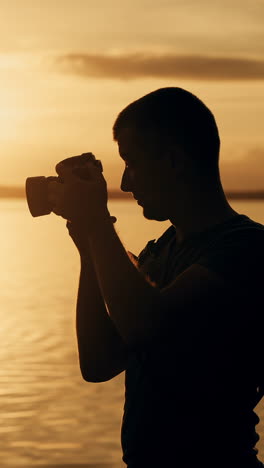 photographer at the top of a hill by the river. beautiful summer sunset. vertical video