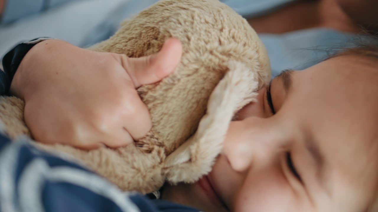 Child hands playing plush toy at bedroom closeup. Little girl embracing animal