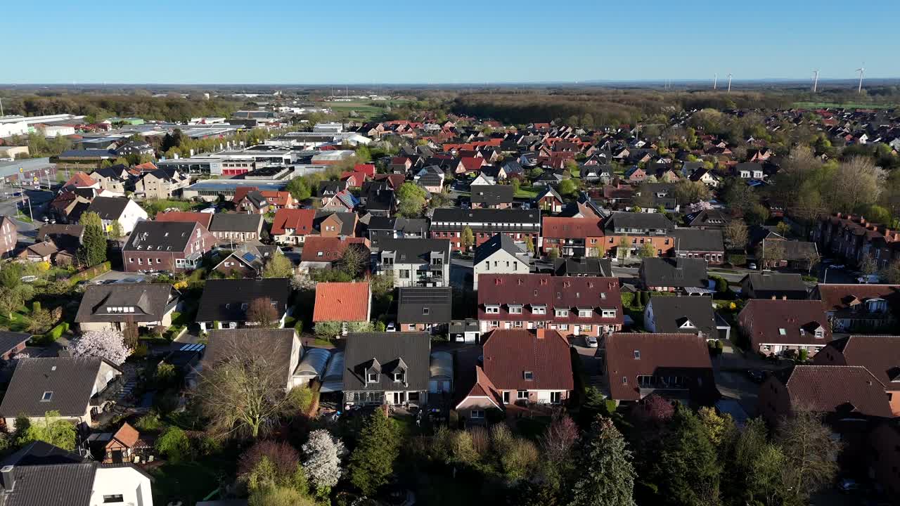 Charming american neighborhood with one Family houses and garden between colored trees.Sunset time in quiet district of city in spring season. Aerial forward wide shot. Wind turbine spin in background