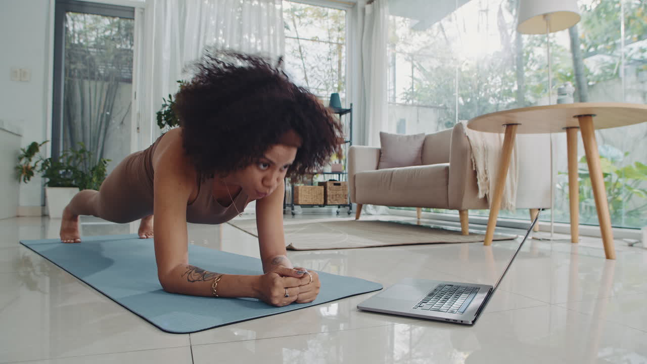 Hispanic Sportswoman Practicing Plank Exercise Using App on Laptop