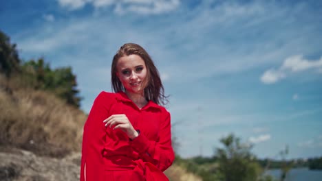 sexy lady outdoors. portrait of a young woman in red dress looking on camera and smiling on the natural background. beautiful female attracts attention by her hand.