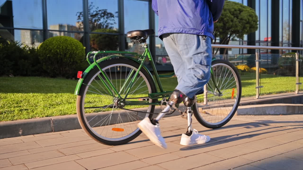 Slow motion view of a man with prosthetic legs. Walking with a bicycle on the street with greenery