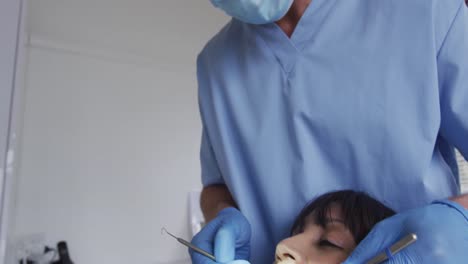 Dentista-Caucásico-Con-Mascarilla-Examinando-Los-Dientes-De-Una-Paciente-En-Una-Clínica-Dental-Moderna