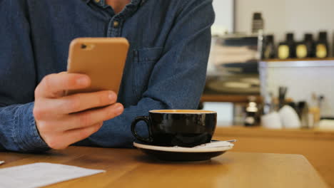 Nahaufnahme-Von-Afrikanischen-Weiblichen-Kellnerhänden,-Die-Einem-Jungen-Kaukasischen-Mann,-Der-Ein-Smartphone-Benutzt,-Eine-Tasse-Kaffee-Servieren