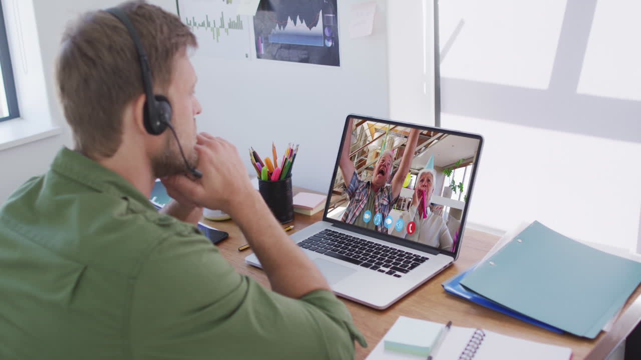 Kaukasisk mand i en videochat på en bærbar computer, iført telefonheadset derhjemme.