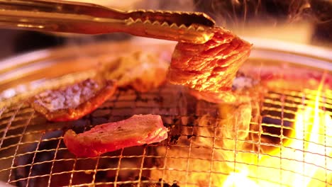 tongs flipping meat on a barbecue grill