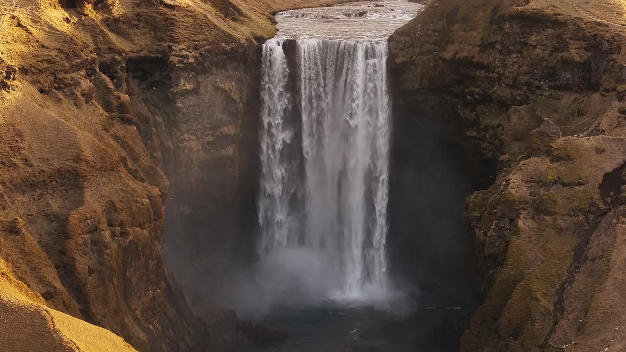 The impressive Skógafoss waterfall in Iceland, fed by the Skógá River, cascades dramatically between steep, rocky banks. Misty spray fills the air. Ideal for travel, nature, powerful natural scenes.