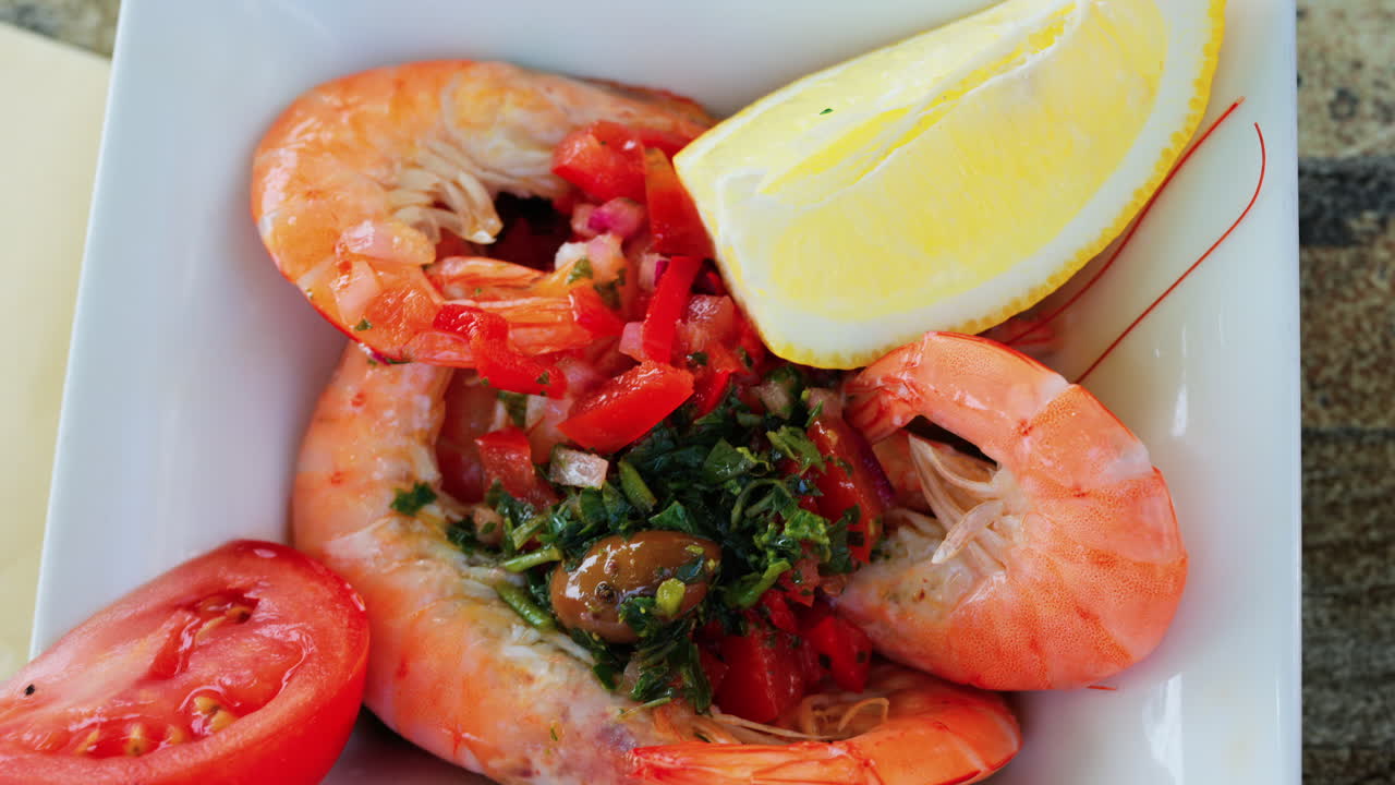 Close up of cooked shrimp with a slice of lemon and herbs on a white plate at a restaurant
