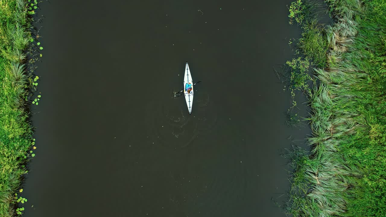 Person kayaking alone on a calm river with green marsh edges in a foldable kayak