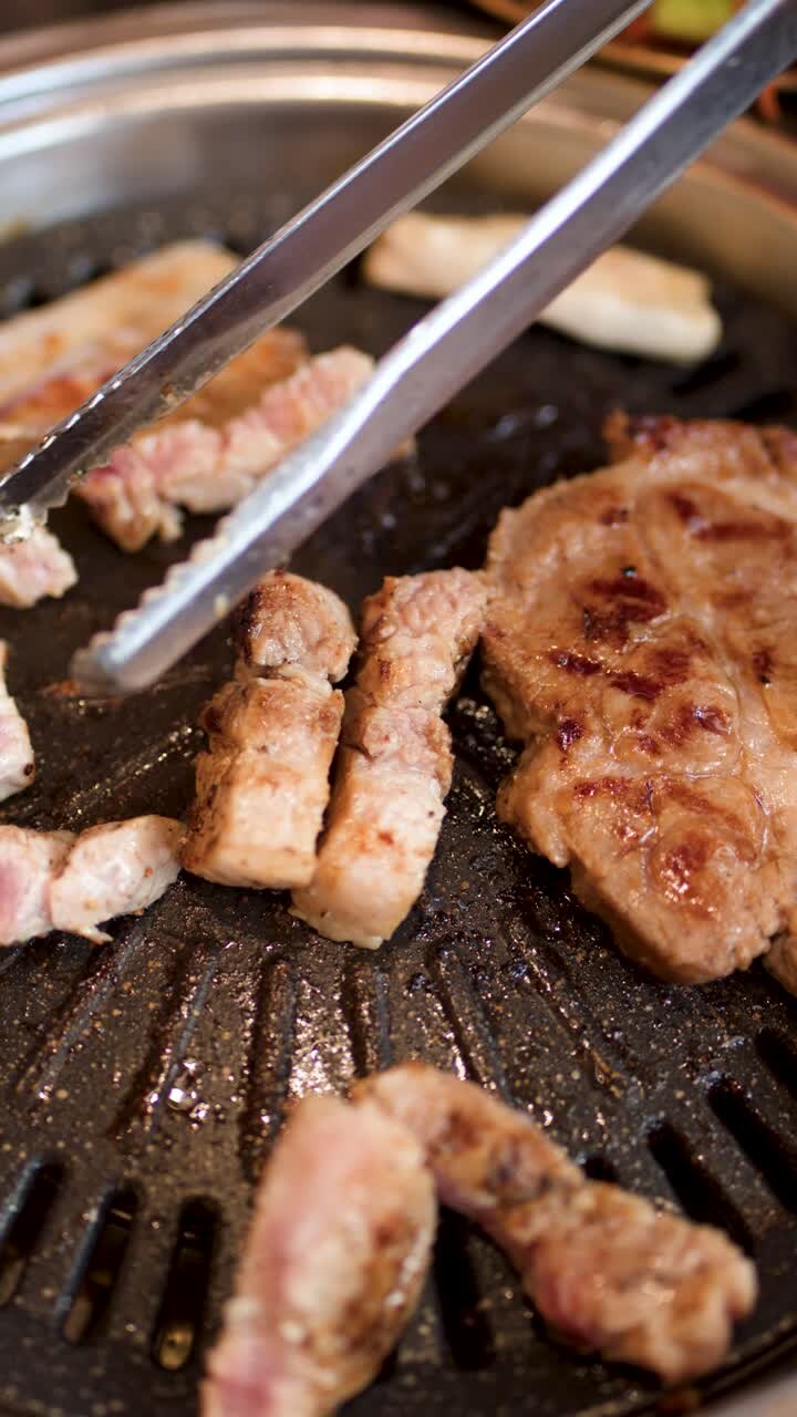 Penjepit memotong dan memanggang irisan perut babi di atas panggangan barbekyu Korea yang panas, tampilan atas.