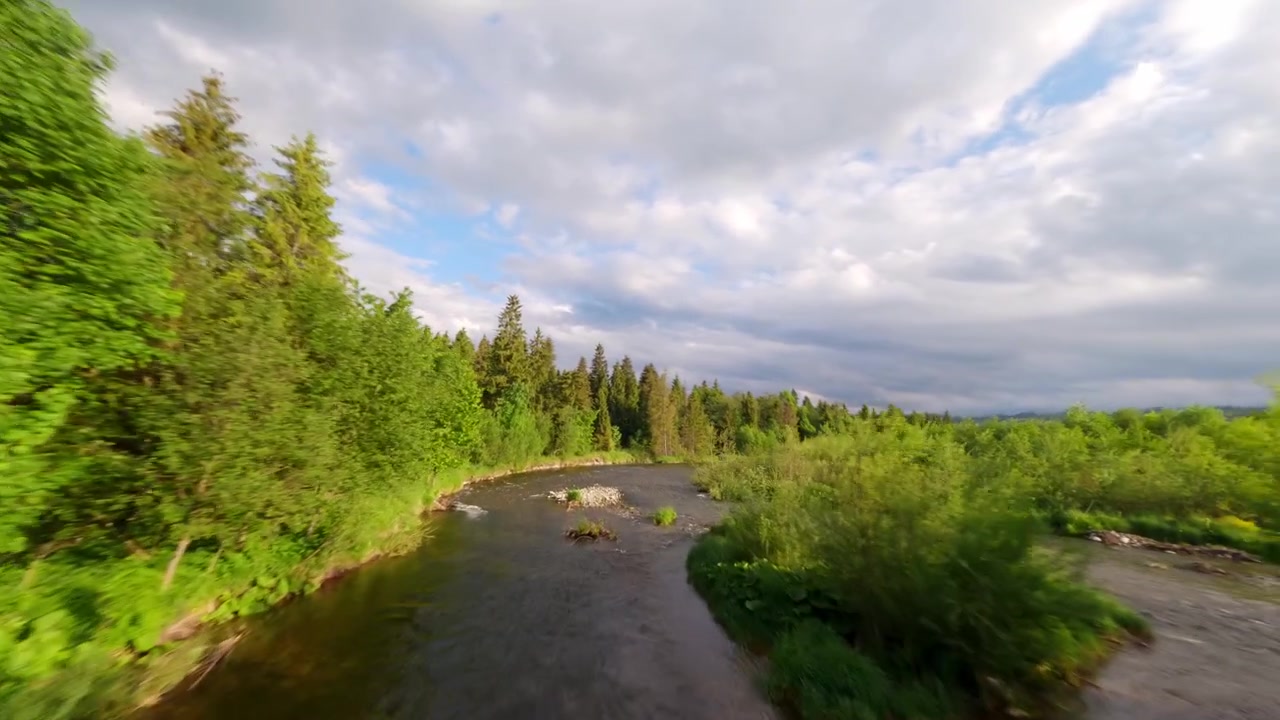 Riprese dinamiche con drone FPV che sorvolano il fiume Biała Tatrzańska, circondato da foreste e prati di un verde vibrante sotto un cielo nuvoloso.