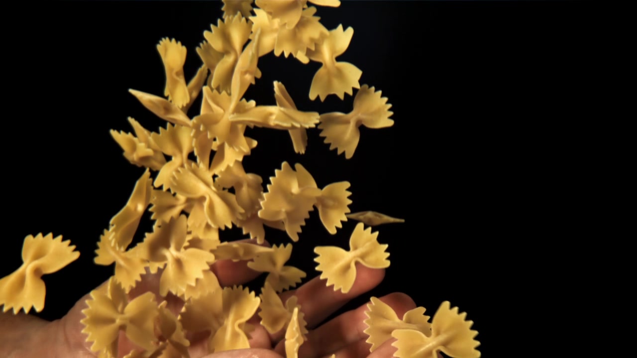 Zeitlupe: Farfalle-Nudeln fallen in gewölbte Hände.