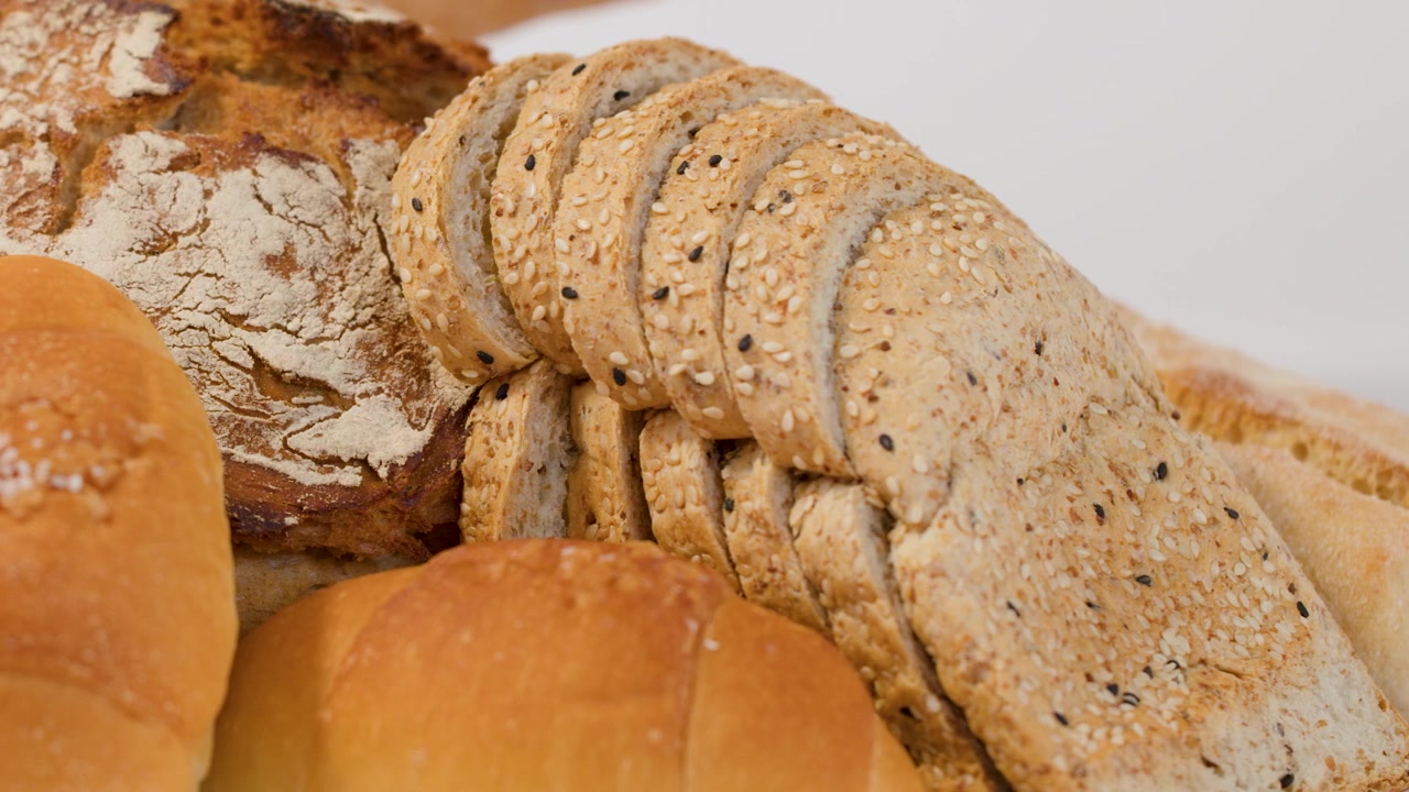 Person Selecting Fresh Bread from an Assortment of Baked Goods