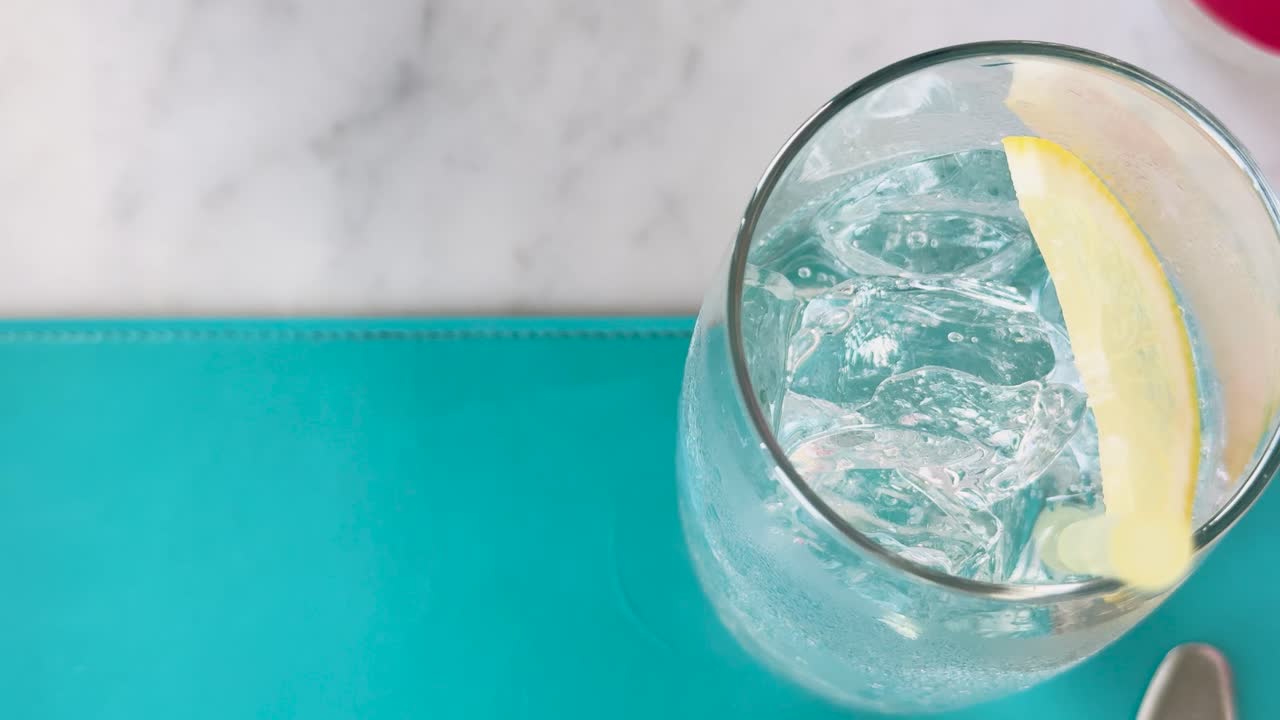 vista superior del club de refresco con rebanada de limón, mostrando burbujas en un vaso transparente en una vibrante superficie turquesa