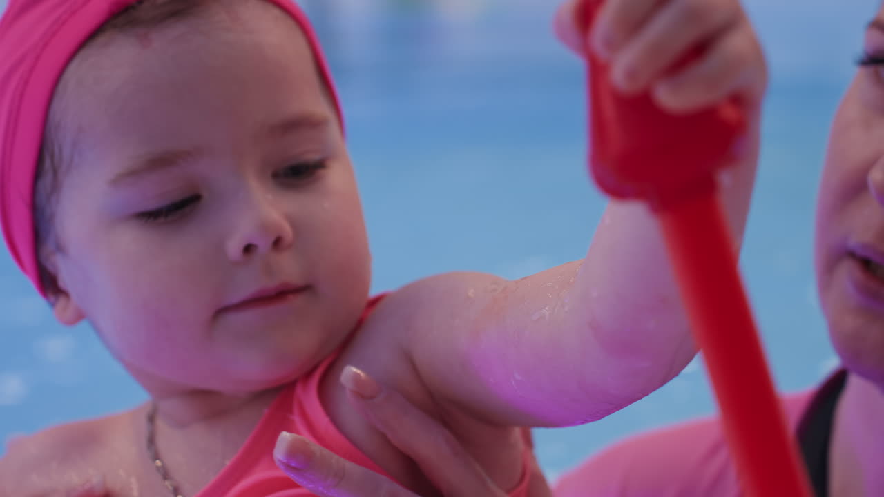 어린 소녀가 풀 누들에 피라미드 장난감을 누르고, 작은 손으로 집중해서 링 스택을 밀고, 수면에는 여러 색깔이 보이며, 노력하는 모습과 쌓여가는 협동심, 차분한 분위기 속에서 즐겁게 초기 기술을 연습하는 모습이 보여요.