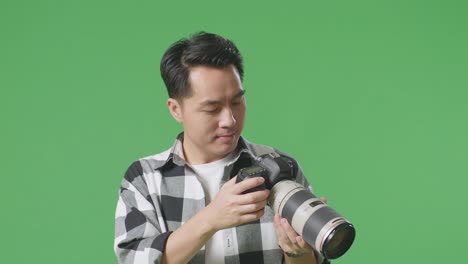 close up of asian photographer looking at the pictures in the camera and showing okay gesture while standing on green screen background in the studio