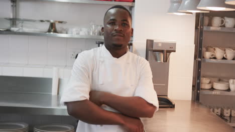retrato de un feliz chef afroamericano cruzando los brazos y sonriendo en la cocina, en cámara lenta
