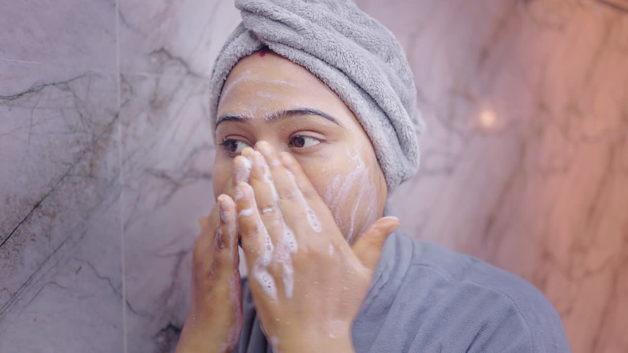 Young woman washing her face with foaming cleanser in bathroom, following daily skincare routine for clean and healthy skin