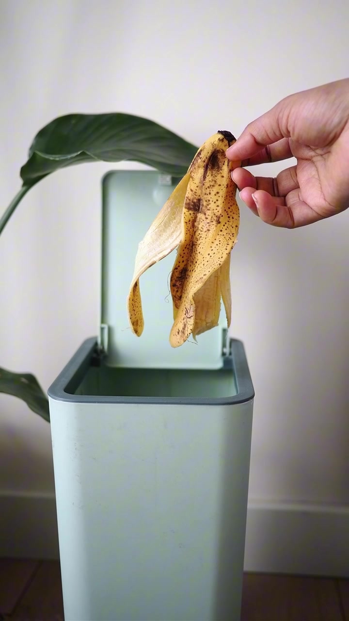 Hand Dropping Banana Peel into a Modern Trash Can