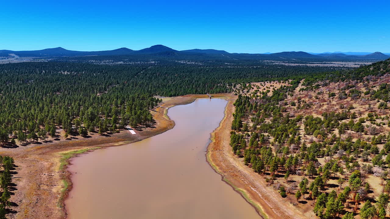 Shallow river flowing through the valley covered with pine tree woods. Mountain range at backdrop. Nature of Arizona State, USA