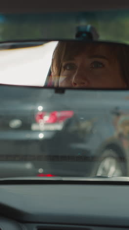 concerned female driver looks in car rear-view mirror to see road condition on back. woman sits in automobile waiting for green traffic light to drive closeup