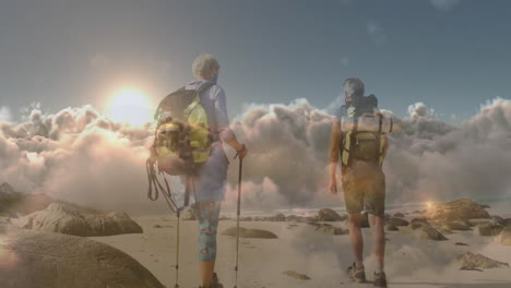 feliz pareja de ancianos caucásicos caminando por la costa con máscara facial sobre nubes que se mueven rápidamente