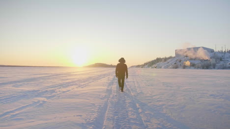 Slow-motion-of-person-walking-on-snow-into-sunset-in-winter,-canada