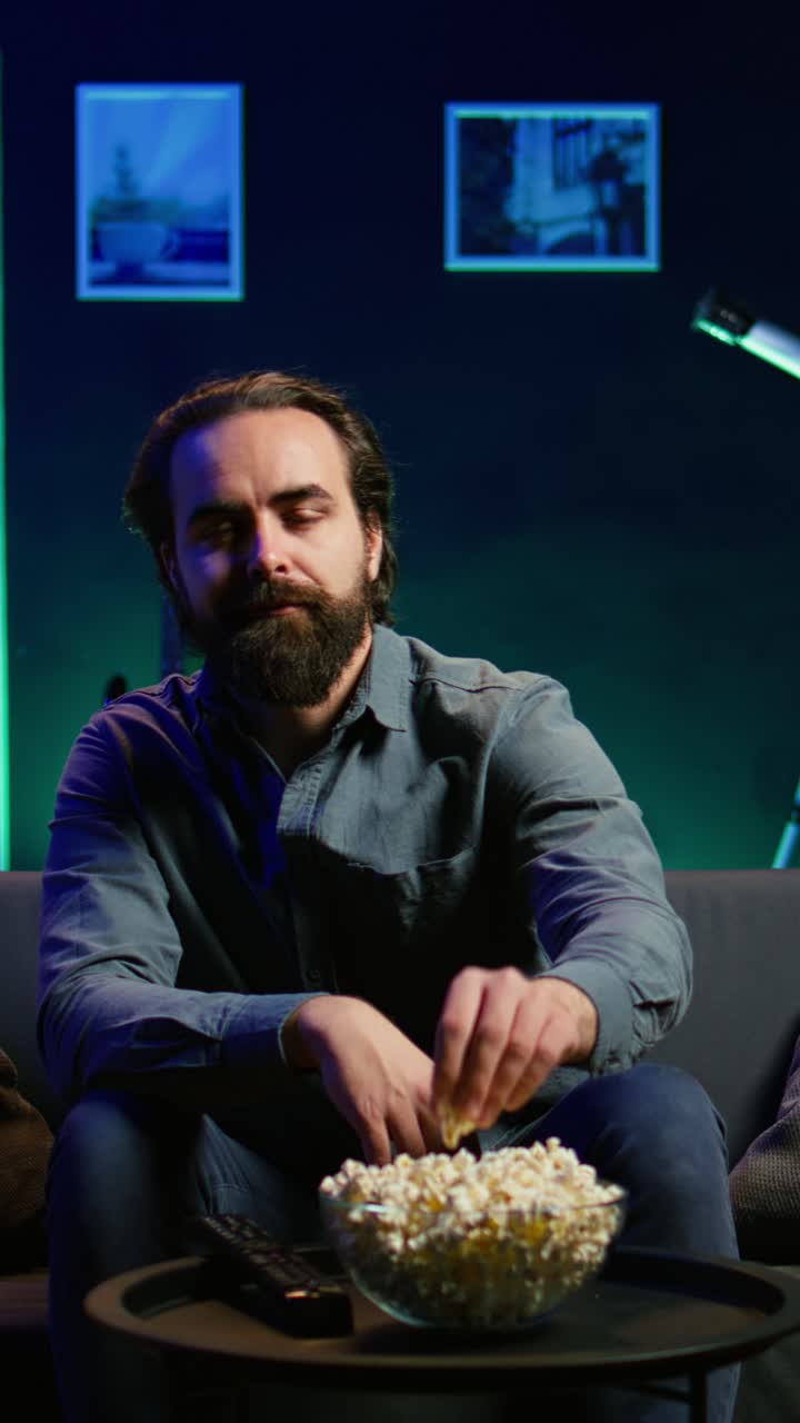 Vertical video Person eating snacks and streaming TV shows in neon lit living room