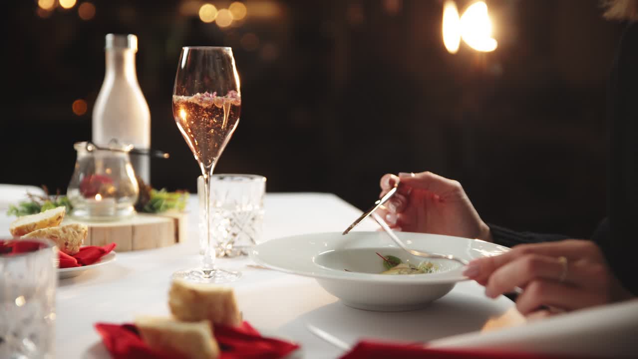 Elegant woman in black takes bit of pasta as champagne bubbles rise in glass with flowers