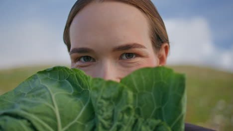 girl examining cabbage closely on field. portrait woman holding lettuce at face