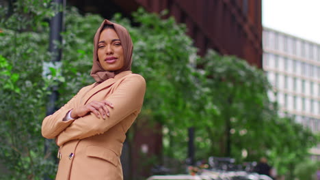 retrato de una mujer de negocios musulmana moderna con hijab y traje de negocios yendo a trabajar de pie fuera de los edificios de oficinas con los brazos cruzados