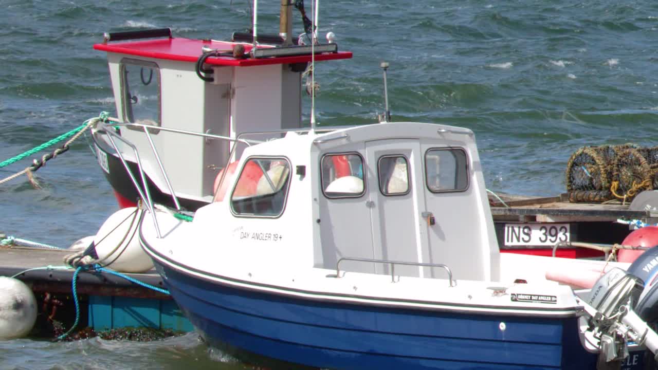 Due piccole imbarcazioni da pesca con motori fuoribordo ondeggiano nelle acque agitate del porto durante una giornata luminosa.