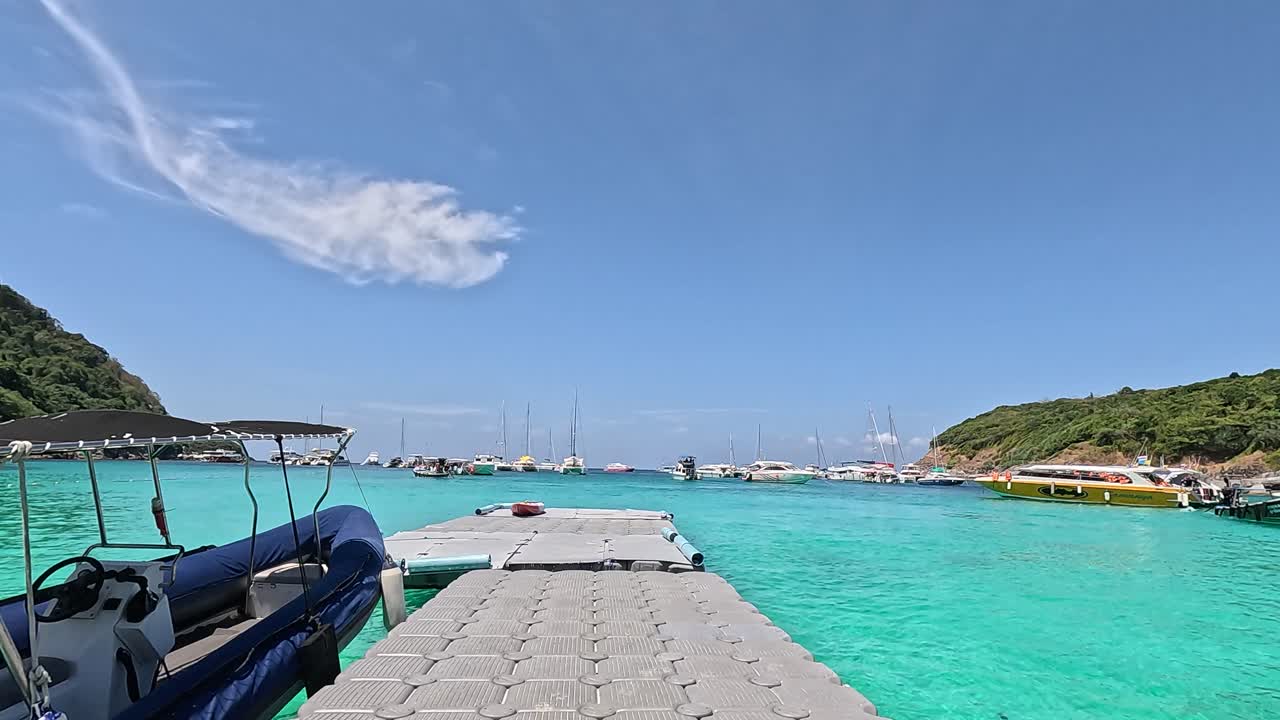 A longtail boat is docked at a floating pier in Phuket, Thailand, under bright daylight with clear turquoise waters