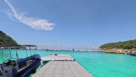 a longtail boat is docked at a floating pier in phuket, thailand, under bright daylight with clear turquoise waters