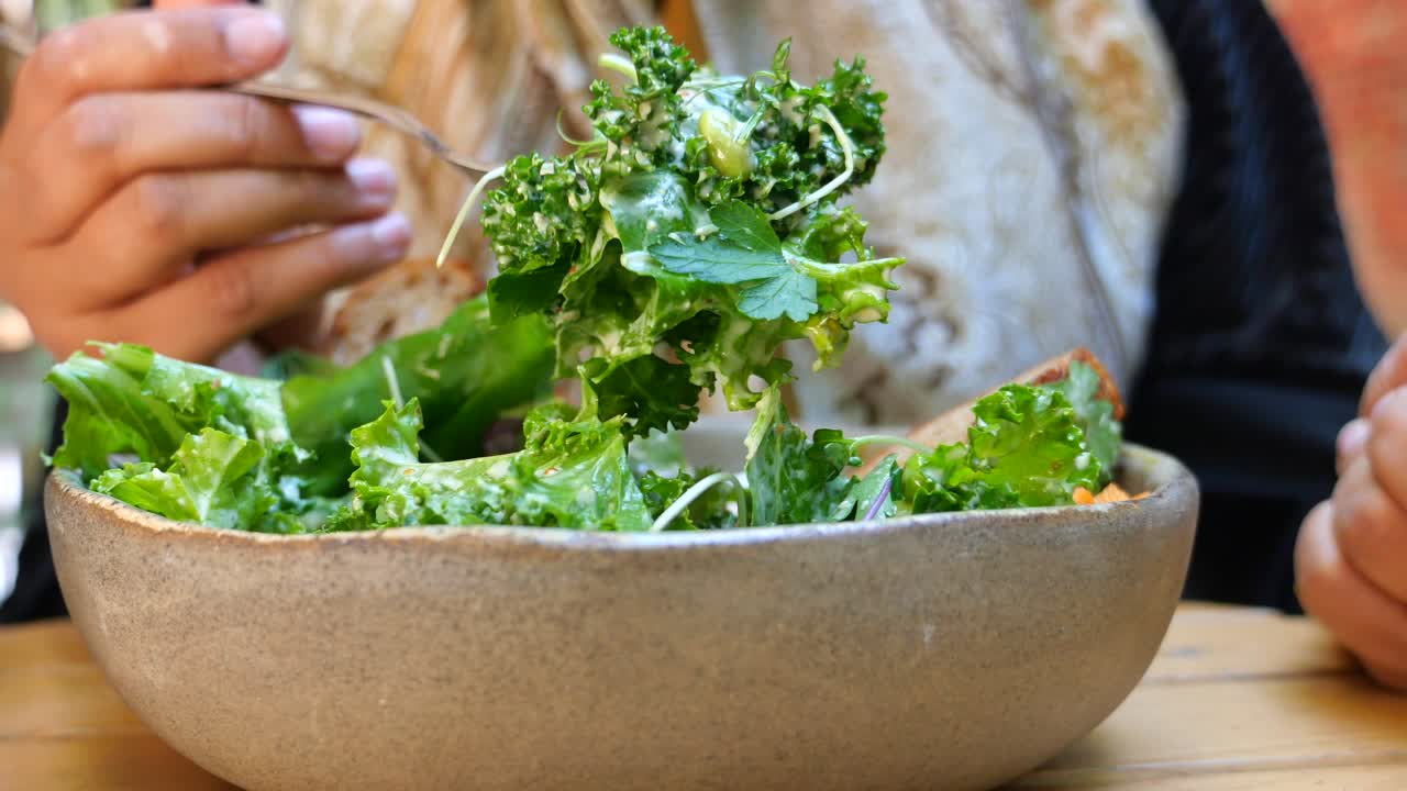 Close-up of a person eating a fresh green salad with kale from a bowl