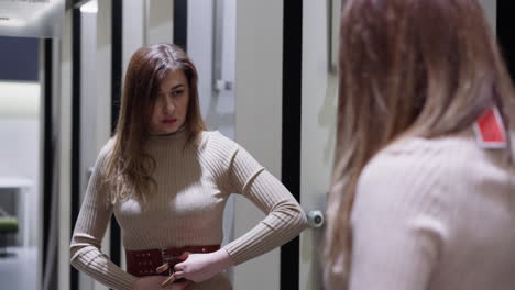 Woman-tries-on-elegant-belt-looking-in-mirror-in-store