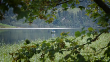 Mann-Fischt,-Während-Er-Allein-Auf-Einem-Schnellboot-Auf-Einem-Riesigen-See-Steht,-Der-Von-Bäumen-Umgeben-Ist