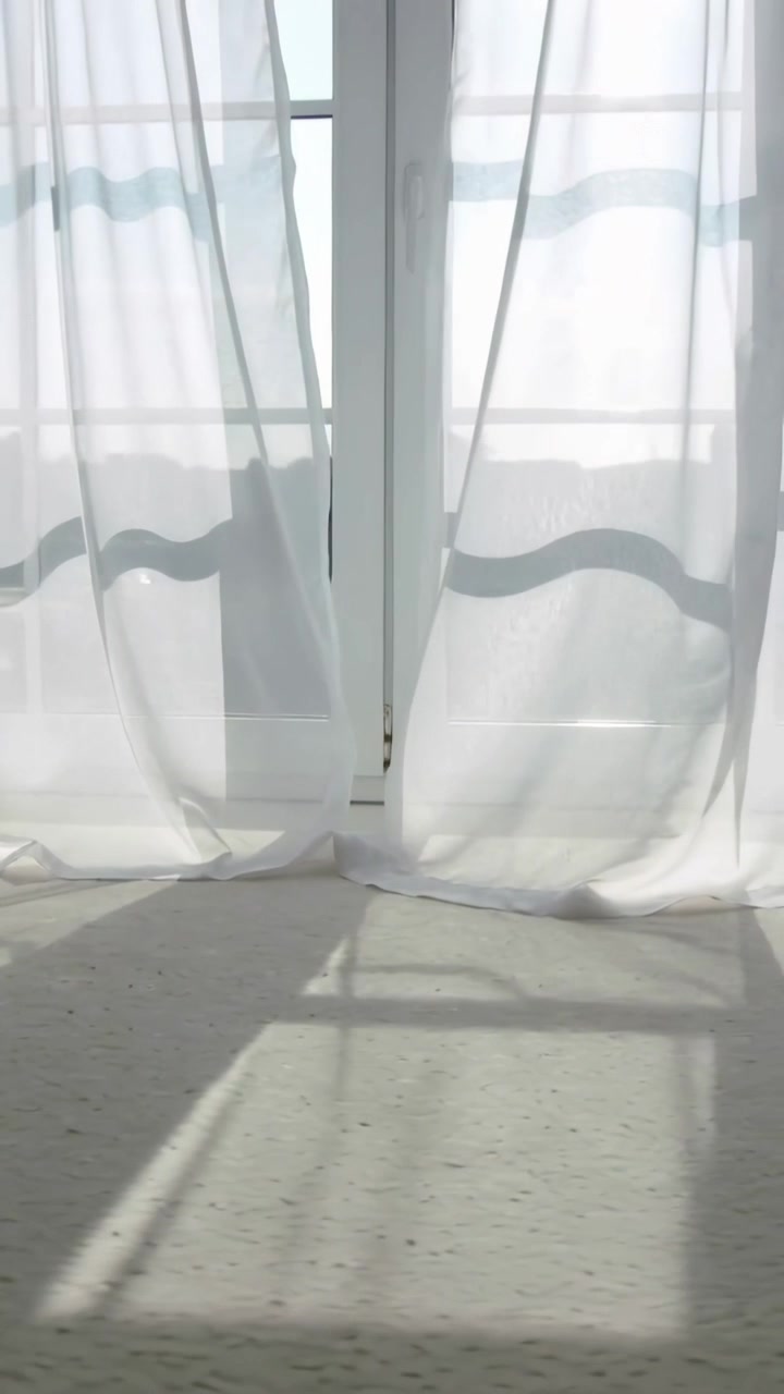 Vertical video: Billowing sheer striped drapes at glass door from breeze, sun making grid shadows